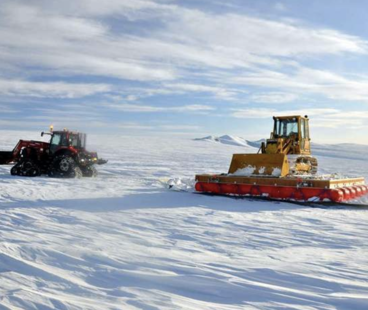 A tractor and snow plow in the middle of a snowy field.